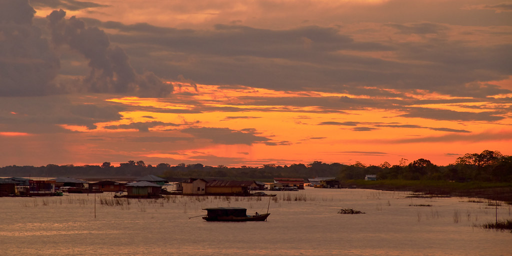 Sunset over the Amazon River in Colombia, with riverside houses and a small boat