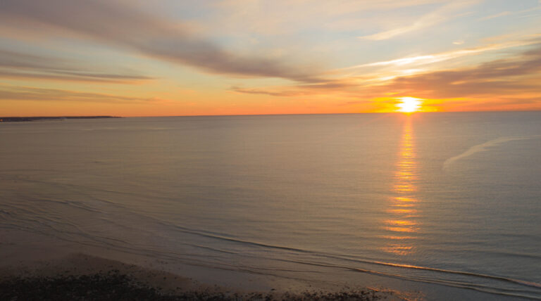 A calm sea at sunset with the sun low on the horizon