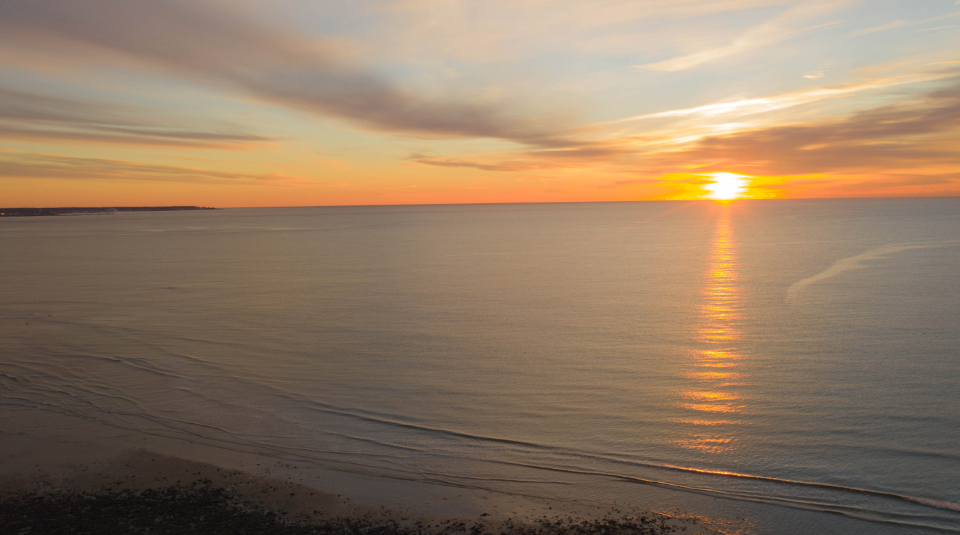 A calm sea at sunset with the sun low on the horizon