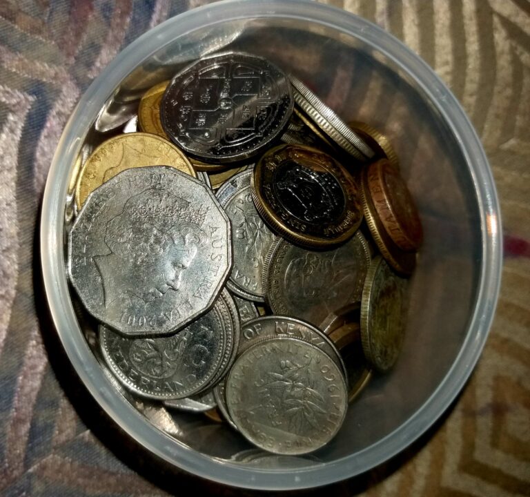A clear jar filled with coins from different countries