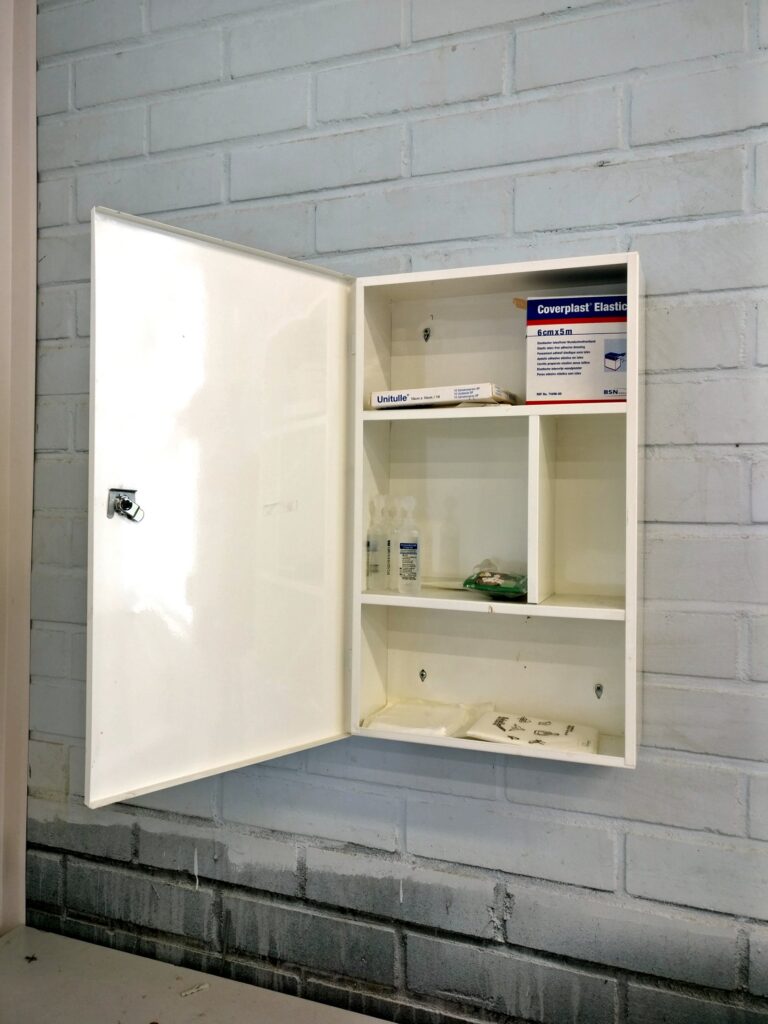 An open first aid cabinet mounted on a painted brick wall