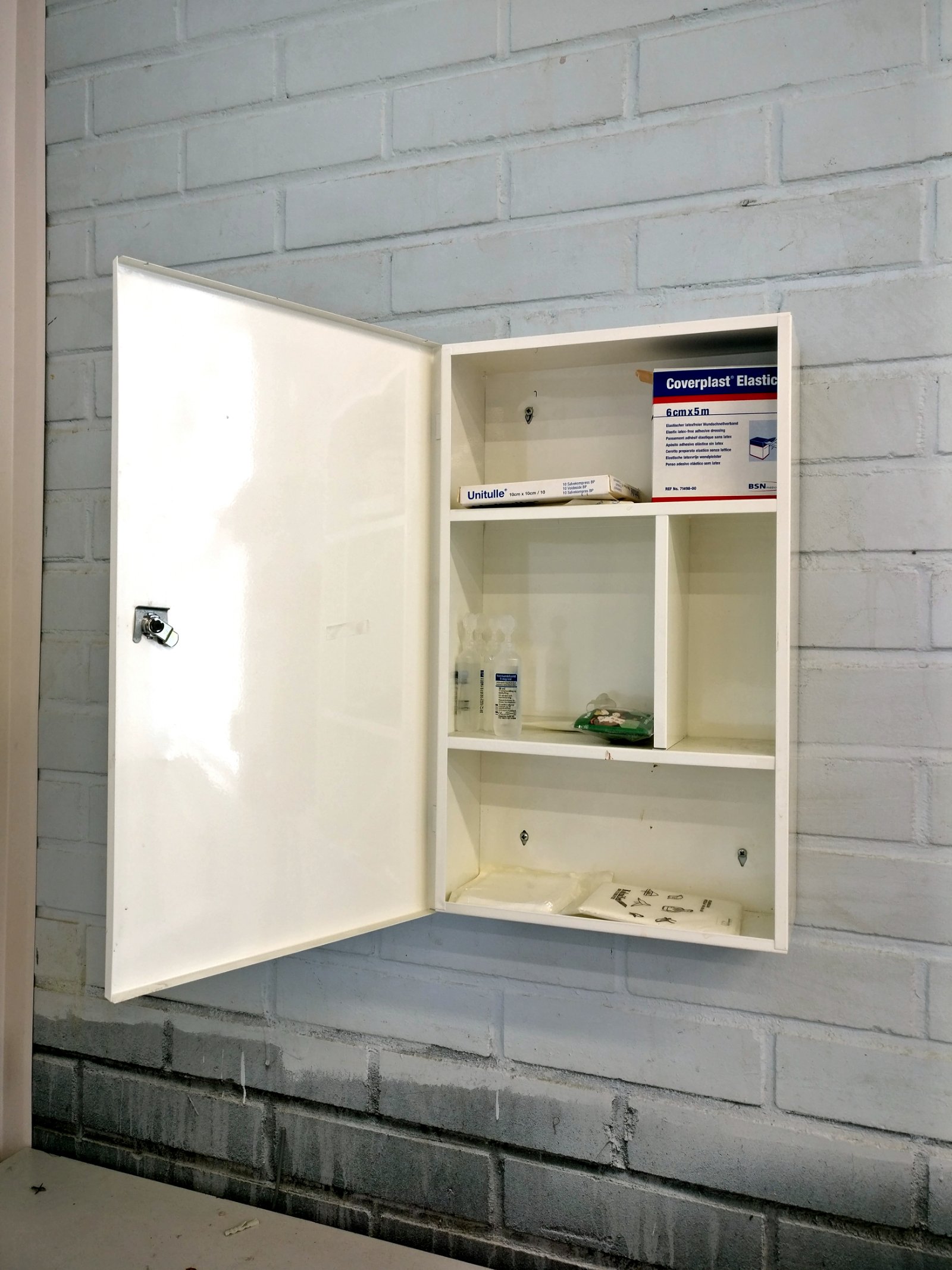 An open first aid cabinet mounted on a painted brick wall