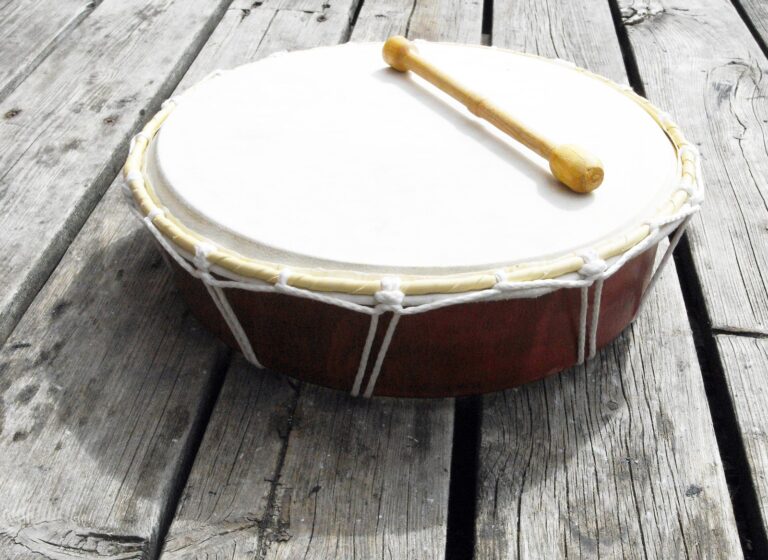 A frame drum with a wooden beater resting on weathered boards