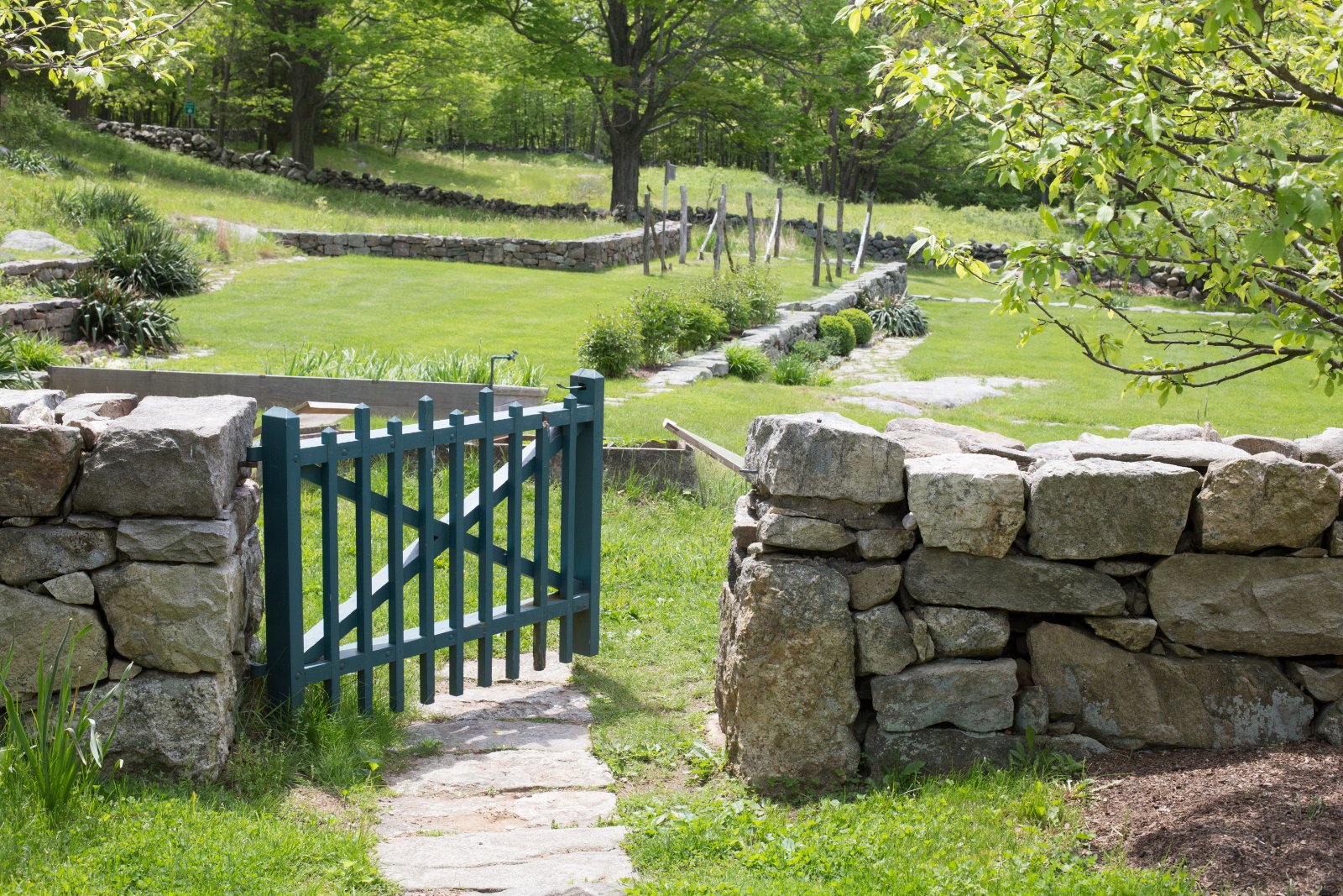A green garden gate standing open in a stone wall, with a meadow beyond