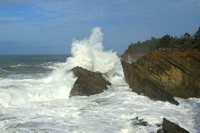 A large wave breaking against dark rocks on the Oregon coast