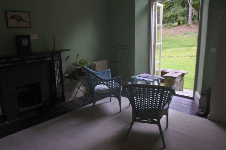 Two wicker chairs in a quiet room beside an open door onto a garden