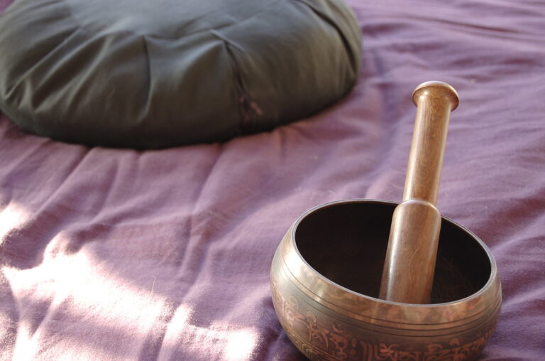 A singing bowl beside a meditation cushion in sunlight