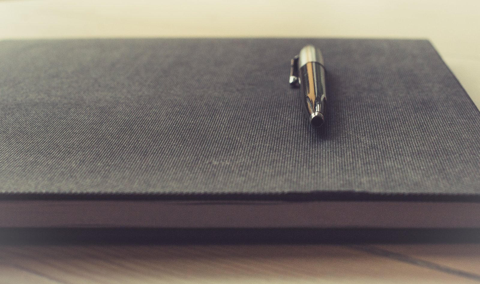 A pen resting on a closed grey notebook