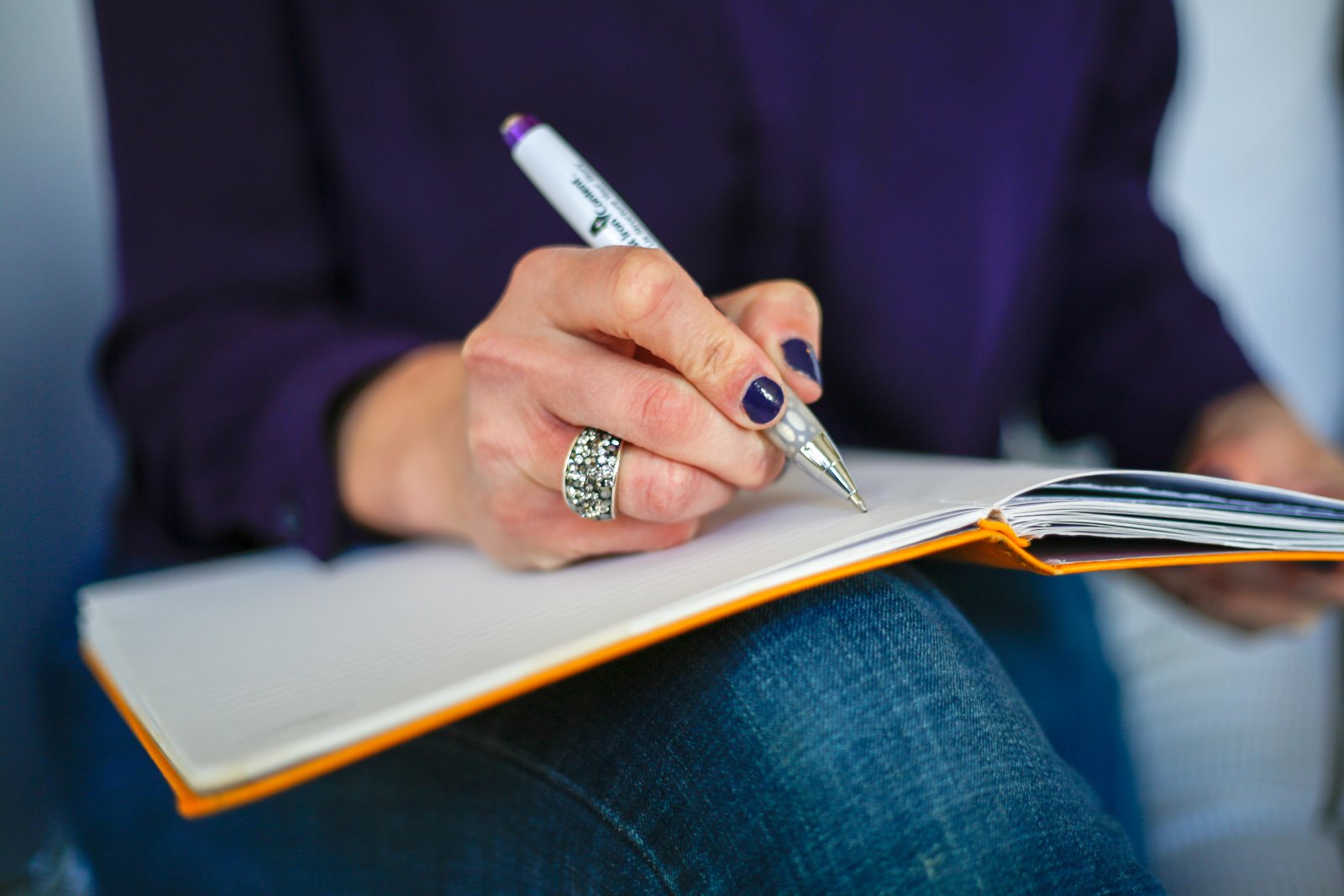A hand writing in an open notebook resting on a knee
