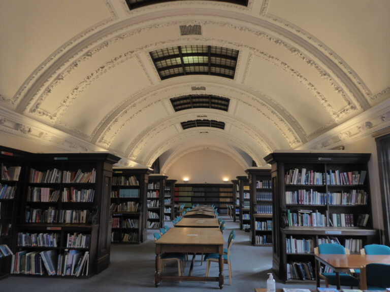 An empty library reading room with bookshelves and long wooden tables under a vaulted ceiling
