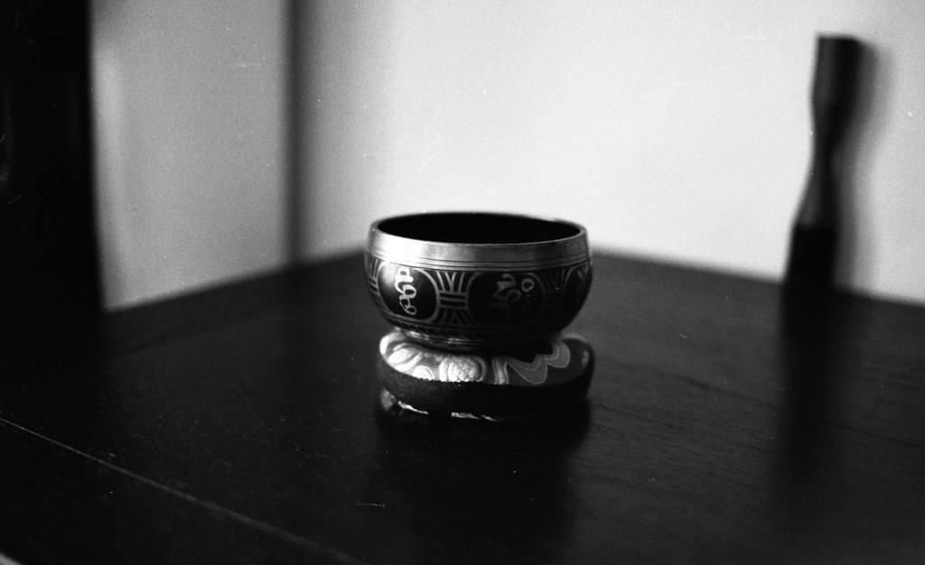 A metal singing bowl on a cushion on a dark wooden table, in black and white