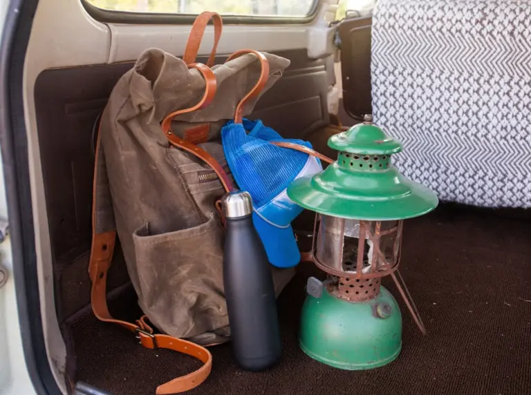 A canvas backpack, a cap, a water bottle and a camping lantern in the back of a car